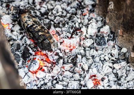Close-up view of glowing red embers and burnt wood charcoal covered in white ash inside an outdoor metal barbecue grill container ready for cooking. I Stock Photo