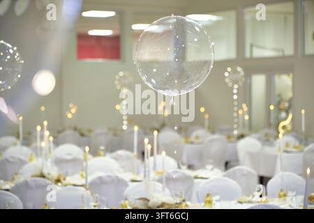 A transparent balloon floats above white-covered chairs and candlelit banquet tables prepared for a ball. Stock Photo