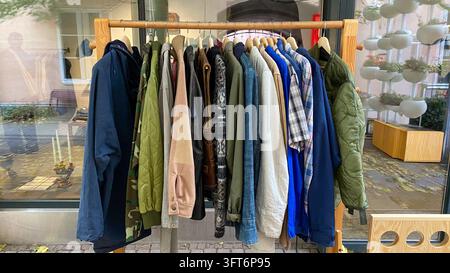 Assorted second hand jackets, coats and shirts hanging on wooden clothing rack at outdoor vintage clothing market Stock Photo