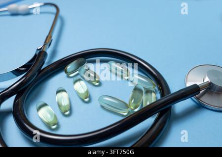 Close-up of a black medical stethoscope surrounding translucent softgel capsules on a light blue background. Healthcare, medication, pharmaceutical an Stock Photo