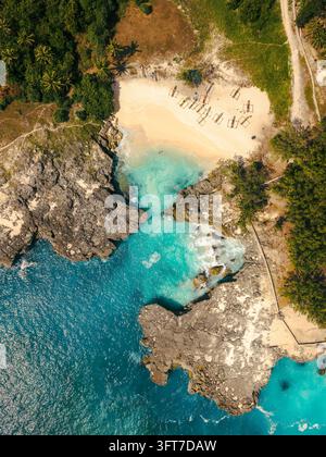 Aerial view of Waikuri Lagoon featuring turquoise waters, rugged limestone cliffs, a sandy beach, and lush tropical vegetation in Kecamatan Kodi Utara Stock Photo