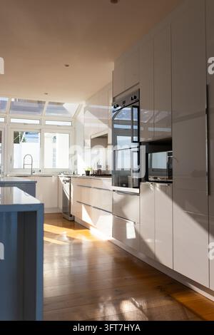 Wall of glossy white cabinets is featuring built-in ovens and microwave in bright modern kitchen Stock Photo