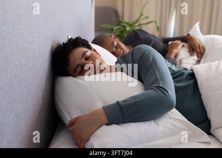 Male partners lying on bed, sleeping with foreground man hugging white pillow in teal shirt. Bedroom, romance, relaxation, calm, cozy, duvet, headboar Stock Photo