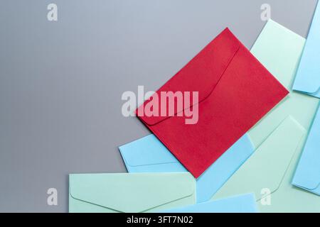 Red envelope on top a pile of blue and green envelopes on a gray background with copy space. Priority mail, urgent message, important notice, direct m Stock Photo