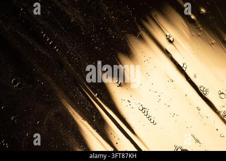 Golden liquid with oil bubbles and water drops creating an abstract texture. Dynamic fluid surface with shiny reflections Stock Photo