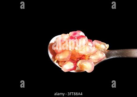 Pomegranate arils on a metal spoon against a black background. Stock Photo