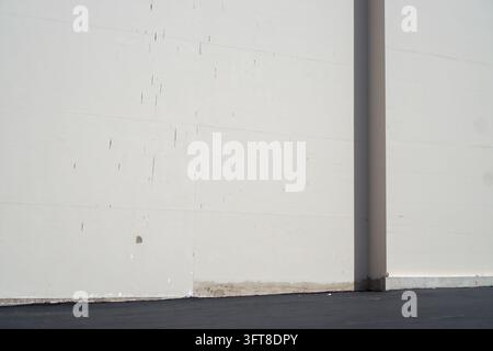 A plain white exterior wall and dark pavement are divided by a broad vertical shadow in bright daylight. Stock Photo