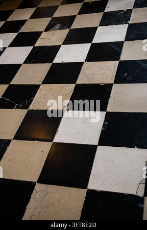 A black and cream checkerboard marble floor forms a geometric pattern of worn square tiles in a Paris interior. Stock Photo