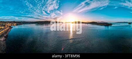 Aerial view of the coastal town of Oban at sunset, featuring calm waters, a scenic shoreline, and distant hills under a vibrant sky in Oban, Scotland, Stock Photo
