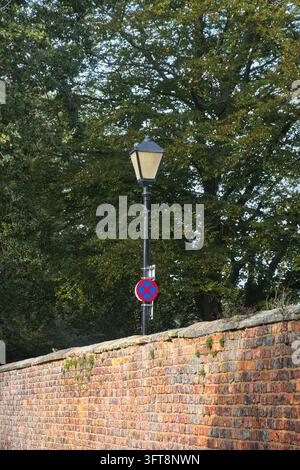 Traditional black street lantern along a public highway and no stopping traffic sign mounted above an old red brick wall. Stock Photo