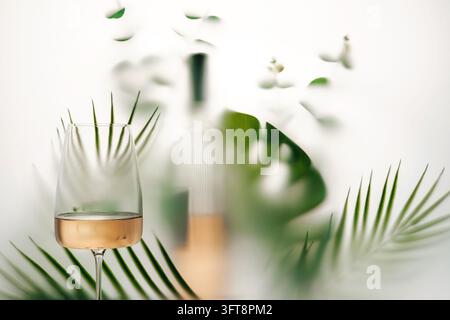Elegant rose wine glass with tropical palm leaves, blurred greenery and ...