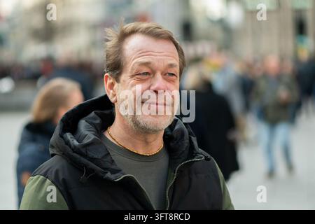 A smiling middle aged man stands outdoors with a blurred crowd behind him. Stock Photo