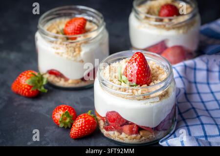 Delicious strawberry magnolia desserts layered with cream pudding and biscuit crumbs in glass jars on dark table Stock Photo