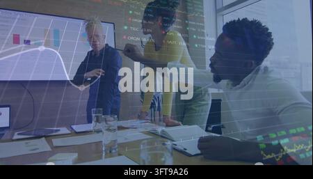 Reviewing three-person team wearing shirts pointing at meeting room display, with stock overlay Stock Photo