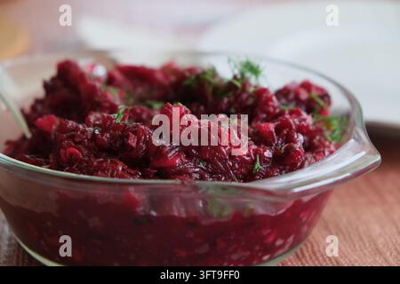 Close up view of traditional homemade grated beetroot salad garnished with dill, served in a clear glass bowl on a table. Healthy vegan appetizer and Stock Photo