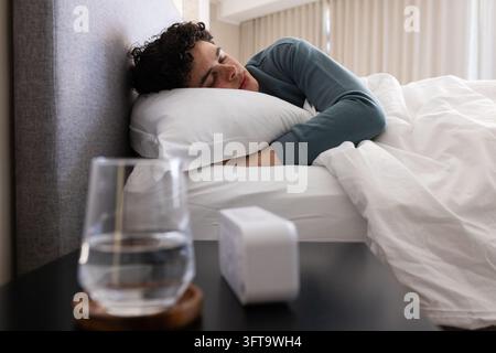 Adult African American man sleeping on side in bedroom with teal top, glass and alarm Stock Photo