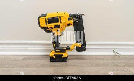 Yellow cordless fastening tool stands upright on a light wood floor against a plain beige wall, with its battery base, magazine, handle, and a loose m Stock Photo