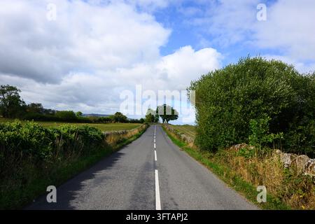 Country road passing between stone walls past agricultural fields in Shropshire England Stock Photo