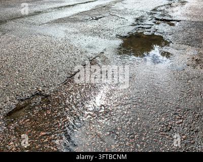 potholes and puddles on wet asphalt road. street road surface after rain. Stock Photo