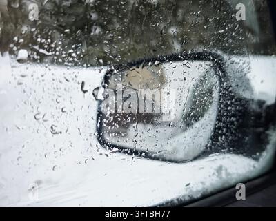 Raindrops on a car window with side mirror. Winter thaw, wet weather, transportation and travel concept Stock Photo