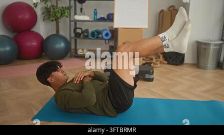 Man lying on mat with legs raised and hands crossed on chest performing abdominal crunch in studio; core strength focus. Stock Photo