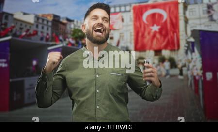 Man tapping smartphone and smiling on street with turkish flag and market booths visible; happiness connection. Stock Photo