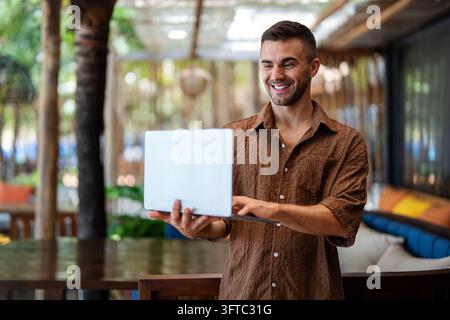 Happy digital nomad programmer working remotely on laptop in a stylish cafe Stock Photo