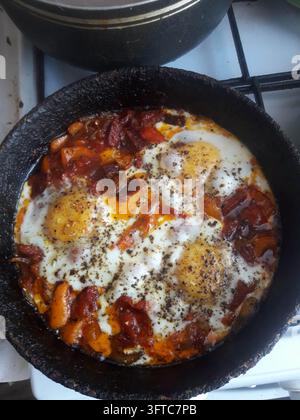 Fried eggs with colorful vegetables cooking in a black kitchen pan Stock Photo