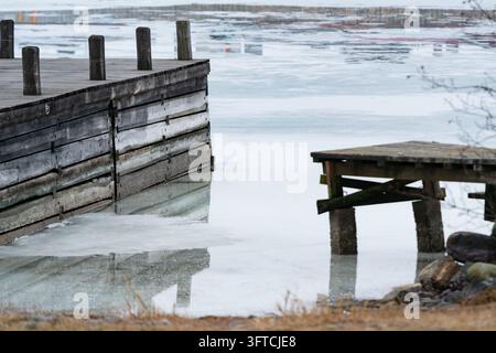 WOODEN PIER IN ICY HARBOUR, REMOTE FINNISH ISLAND IN DEEP WINTER, UTÖ, FINLAND: A weathered wooden pier and a smaller jetty stand in the calm, icy water of a quiet harbour in winter. INFO: Utö is a remote Finnish island in the Archipelago Sea, south of Turku. Known for its historic lighthouse, rugged coastal scenery and maritime heritage, it is Finland’s southernmost inhabited island, attracting visitors seeking tranquillity, birdwatching and spectacular Baltic Sea landscapes. Stock Photo