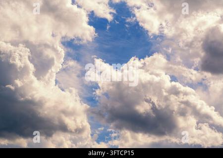 Dramatic blue sky filled with large cumulus clouds and sunlit highlights, creating a textured, atmospheric scene that evokes calm, wonder and shifting Stock Photo