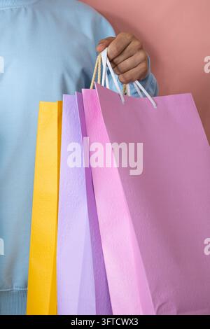 Close up of a man in a blue jumpsuit holding several multicolored shopping bags on a pink background, shopping concept Stock Photo