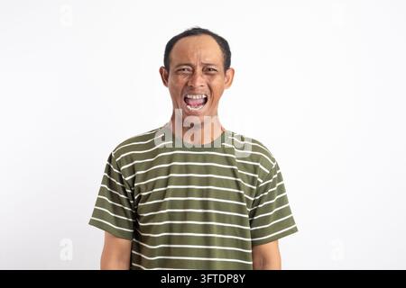 Head shot of angry man shouting and looking with hatred, standing mad against blue background Stock Photo