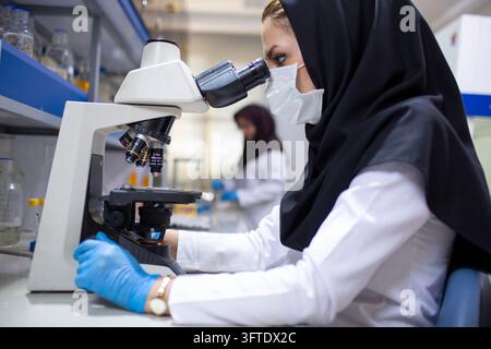 An Iranian Hijab-wearing laboratory scientist carefully examines a specimen through a microscope Stock Photo