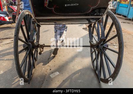 Low angle view of a black hand pulled rickshaw with big spoked wheels and the puller walking barefoot, West Bengal, Kolkata, India Stock Photo