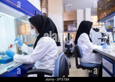 Two female researchers in protective lab gear conduct experiments, using a pipette and microscope in a modern laboratory Stock Photo