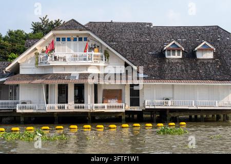 Bangkok, Thailand January 20, 2026. A weathered white wooden building with balconies and shuttered windows stands on piles above the river. Stock Photo