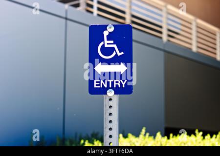 Close-up photograph of a blue wheelchair accessibility sign featuring the international wheelchair symbol and bidirectional arrows indicating accessib Stock Photo