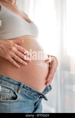 Vertical Photo of Pregnant Woman Applying Belly Cream for Stretch Mark Prevention and Skincare Stock Photo