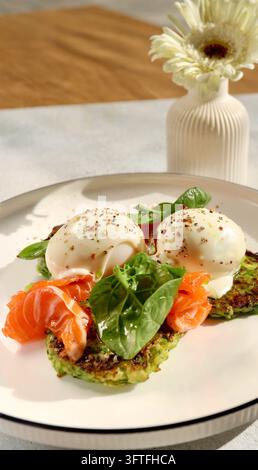 Healthy breakfast on a white flat plate: zucchini fritters, poached egg, salmon and spinach leaves. Natural morning light Stock Photo