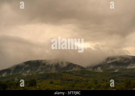 Dramatic stormy sky with rain clouds looming over green mountain hills and valley. Stock Photo