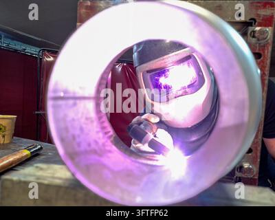 View through round metal pipe of welder working with bright electric arc in workshop Stock Photo