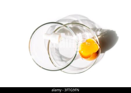 Clear glass tumbler lies on its side around a broken raw egg, with orange yolk visible against a white surface and strong shadows. Clean Ingredient Ae Stock Photo