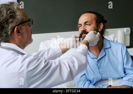 Middle Aged Doctor Examining Middle Aged Patient in Hospital Bed Stock Photo