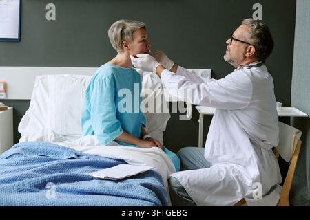 Middle Aged Male Doctor Examining Female Patient in Hospital Ward Stock Photo