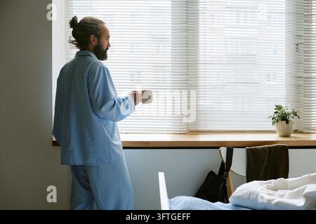 Middle Aged Patient Holding Cup Looking through Hospital Window Stock Photo
