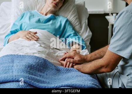 Male Doctor Holding Hand of Female Patient in Hospital Bed Stock Photo