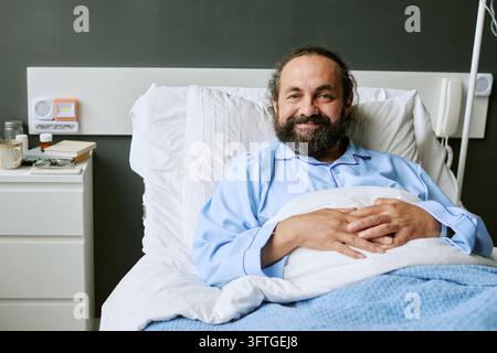 Portrait of Happy Middle Aged Male Patient in Hospital Bed Stock Photo