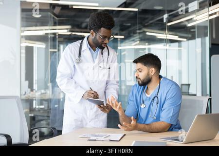 Two diverse medical professionals, a doctor and a nurse, discussing and reviewing healthcare records while working together at a modern hospital or cl Stock Photo
