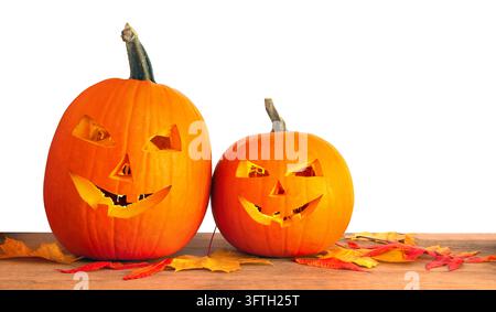 Two festive carved orange pumpkins with joyful smiling jack-o'-lantern faces and fallen yellow and orange maple leaves on a rustic wooden table Stock Photo