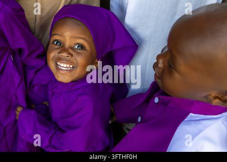 Laughing child in a purple hooded robe looking up beside another child in the Kibera area, Nairobi County, Nairobi, Kenya Stock Photo